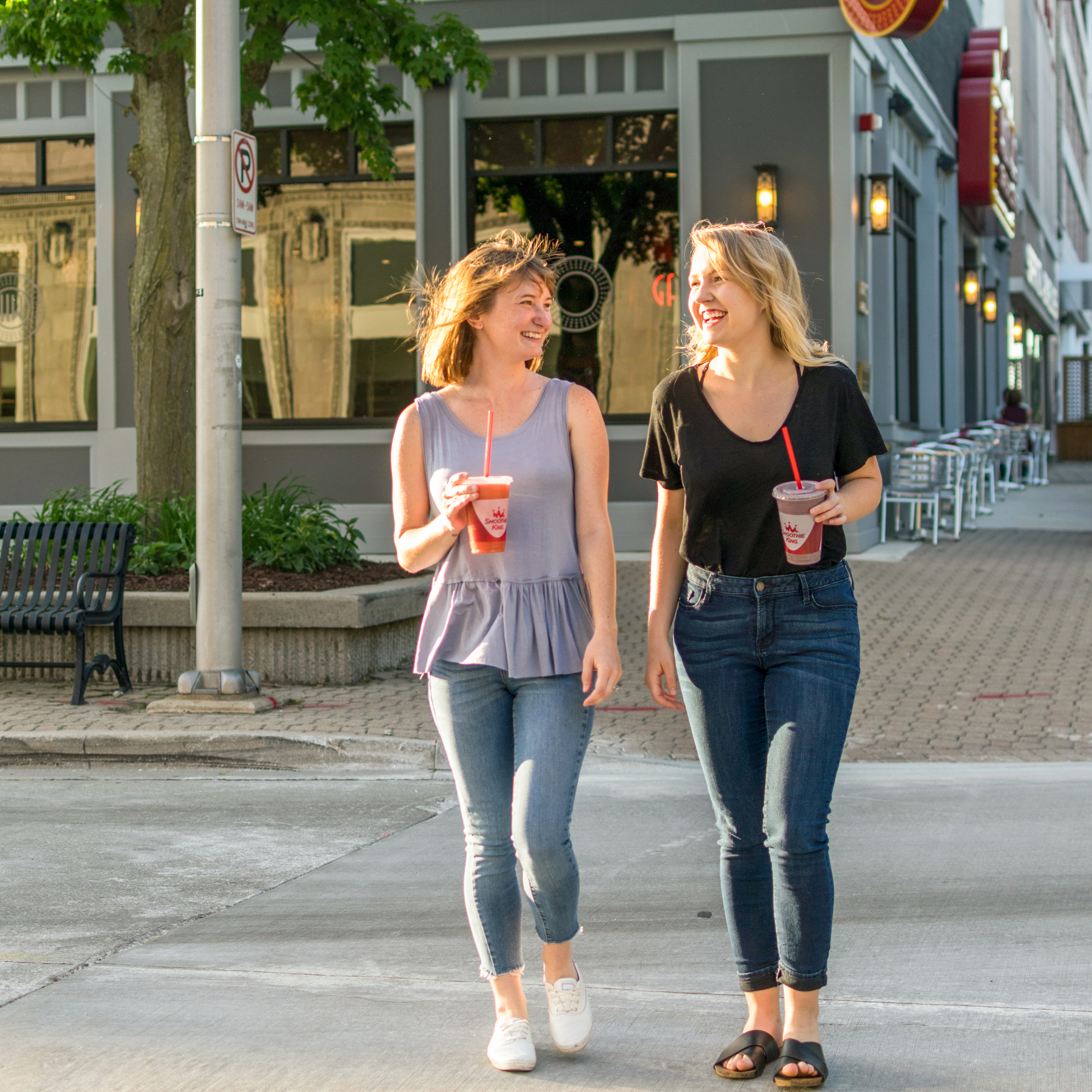 Two women walking in the city with Smoothie King in their hands