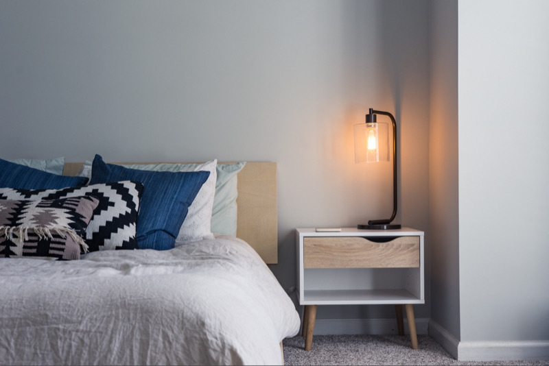 Made bed with end table and ignited lamp