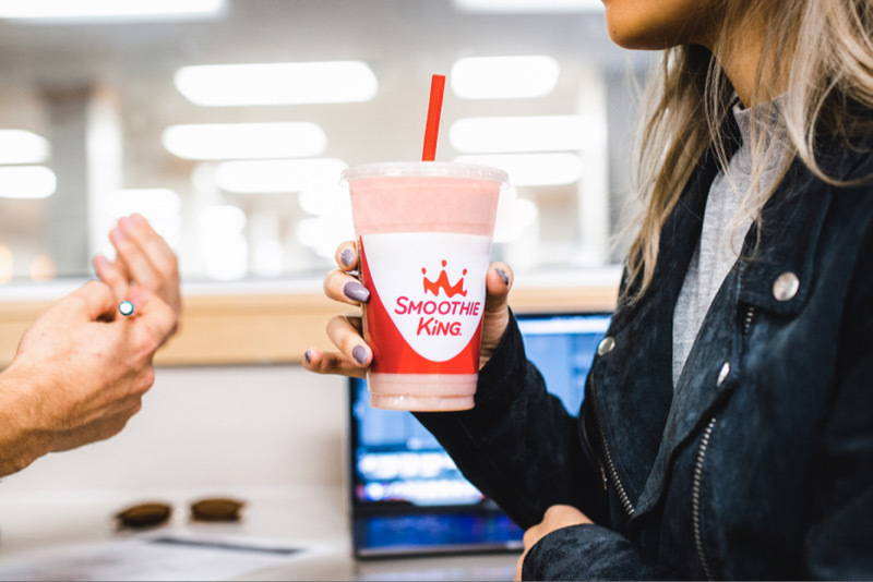 A woman drinking a Smoothie King smoothie with healthy smoothie ingredients while talking to someone at work