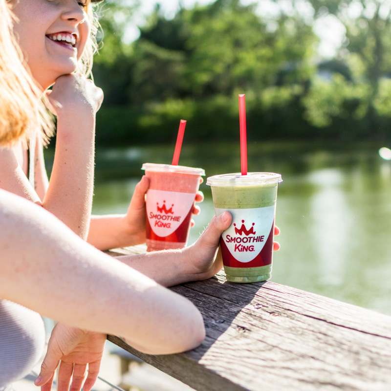 Two friends enjoying healthy smoothies for weight loss near a pond on a sunny day