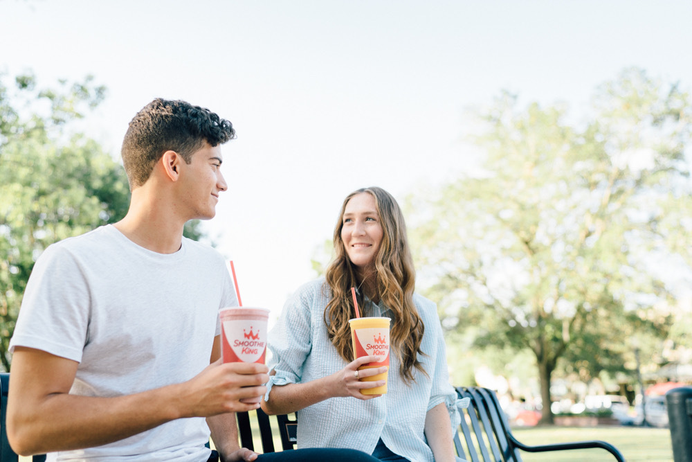 A boy and girl sitting on a park bench drinking Smoothie King protein smoothies